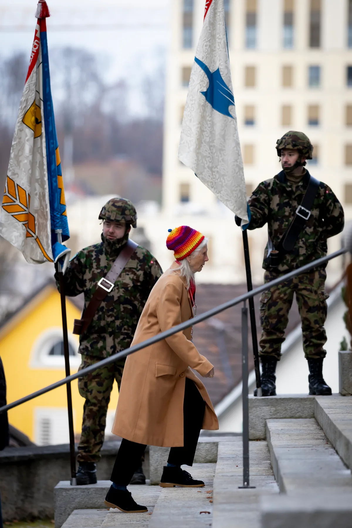 Durch die noch ungewohnten kalten Temperaturen… Eine Frau schreitet die von uniformierten Unteroffizieren bewachte Treppe empor.